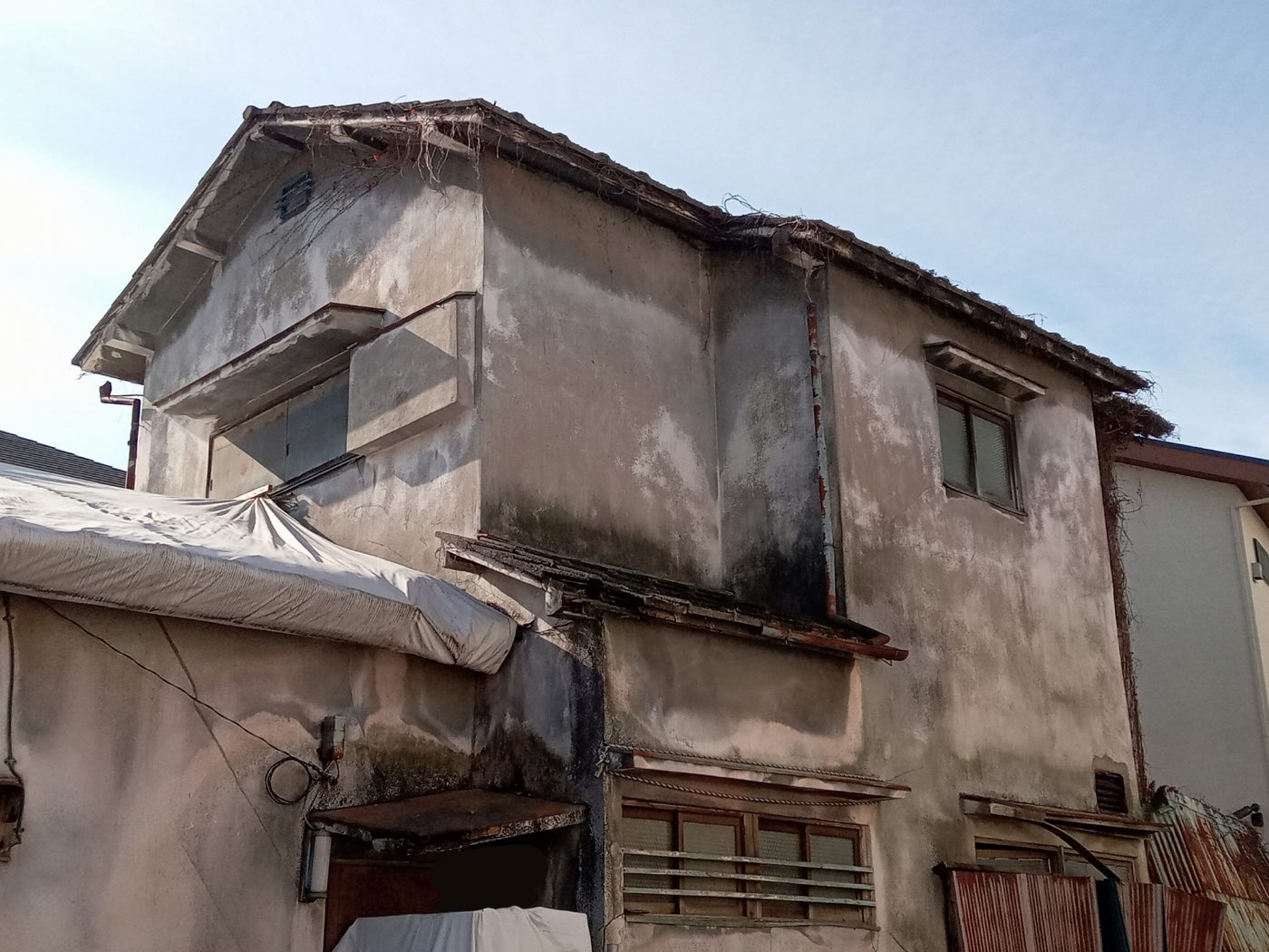 外壁の傷みが目立つ、路地沿いの古い木造2階建て住宅